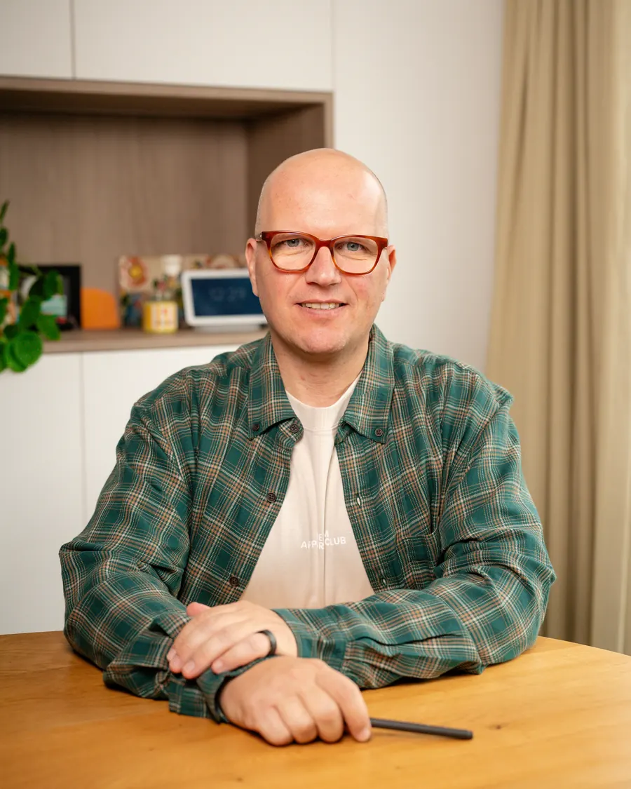 Jan Jacobs aan tafel in zijn praktijk in Mechelen, glimlachend, in een geruit hemd