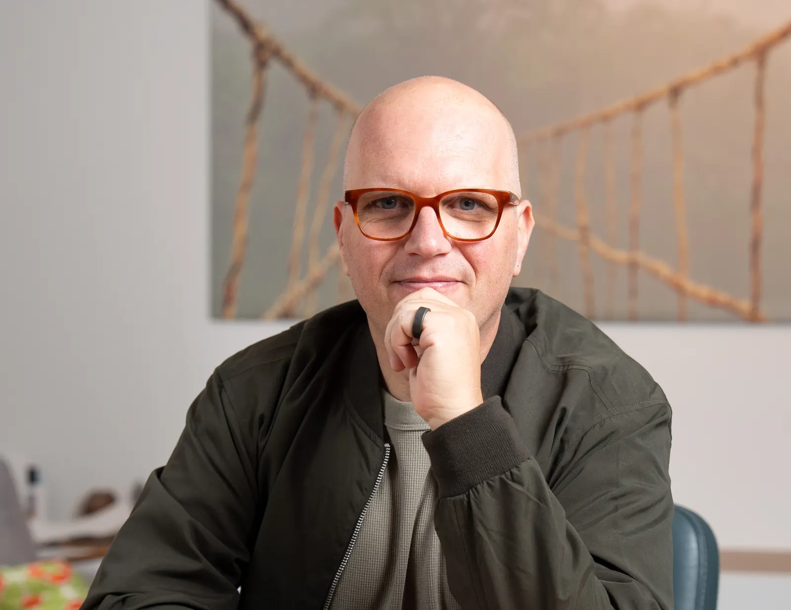 Jan Jacobs in zijn spreekkamer in Mechelen, met het schilderij van de hangbrug achter hem